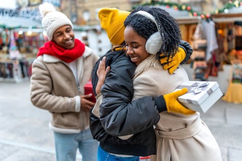 Happy friends exchanging christmas gifts and hugging at a christmas market during winter holidays