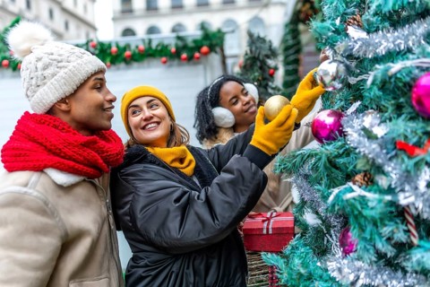 Happy multi ethnic friends decorating christmas tree at outdoor christmas market, wearing winter