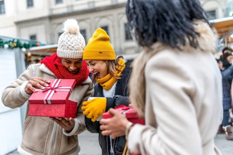Happy friends joyfully exchanging christmas gifts at a bustling market, celebrating the festive