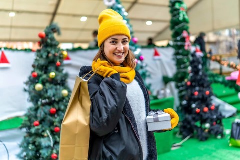 Young woman holding christmas present and shopping bag, enjoying shopping at christmas market