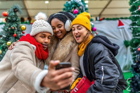 Three cheerful young friends taking a selfie with smartphone in a christmas decorated shopping mall