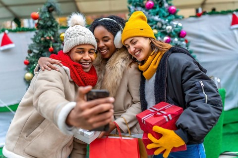 Group of cheerful multi ethnic friends taking a selfie with a smartphone after winter shopping at a