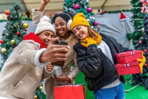 Happy multi ethnic friends taking a selfie after a christmas shopping spree, holding gifts and