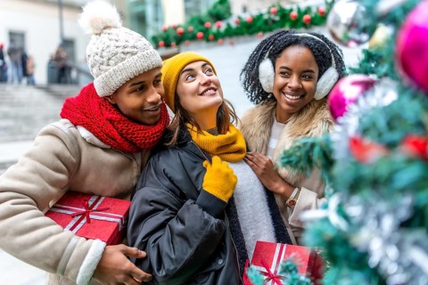 Happy multi ethnic friends holding christmas gifts and enjoying christmas time together outdoors