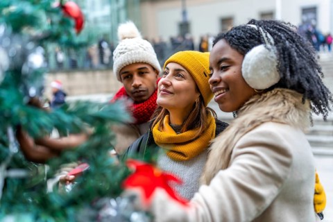 Three friends admiring christmas decorations on a city tree during winter holidays, enjoying time