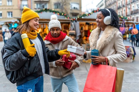 Happy friends exchanging gifts and enjoying hot drinks at a christmas market during winter holidays