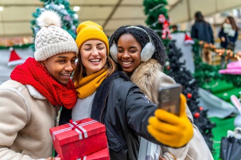 Happy multi ethnic friends taking a selfie at a christmas market, holding presents and shopping