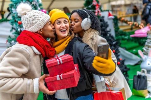 Three happy friends kissing a girl holding christmas gifts and taking a selfie at a christmas