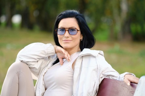 Cheerful woman enjoys a peaceful afternoon in a park, wearing sunglasses and a light jacket. She