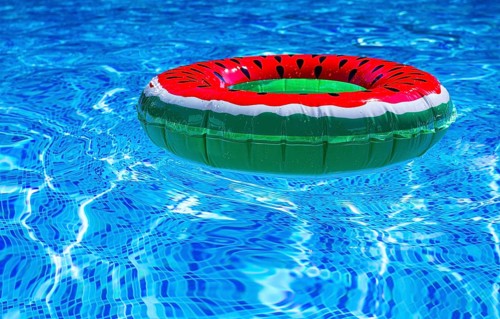 A bright ring-a float, with a watermelon, in the clear blue water of the pool, under the sunlight