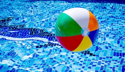 Colorful beach ball floats on the surface of a pool reflecting sunlight on a summer day