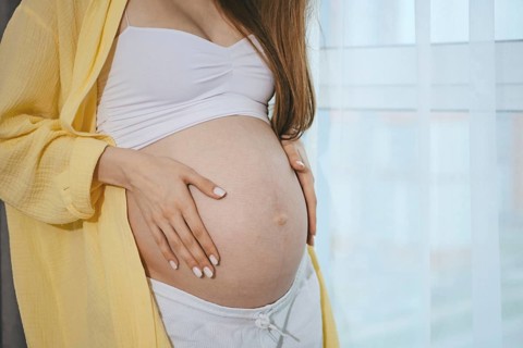 Close-up view of a baby bump of pregnant woman by the window. A woman lovingly places her hands on