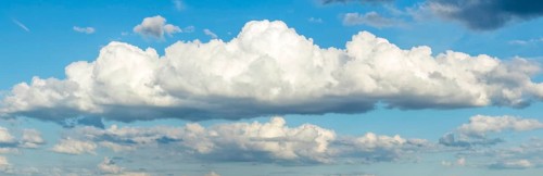 Panoramic photo of long white stratocumulus cloud, in the background more cumulus clouds,