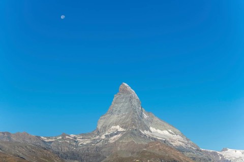 The iconic Matterhorn stands high above a clear evening sky illuminated by a bright moon. This