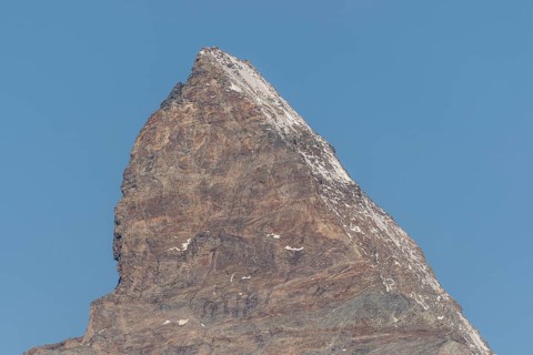 A towering Matterhorn mountain peak stands prominently against the clear blue sky, revealing rocky