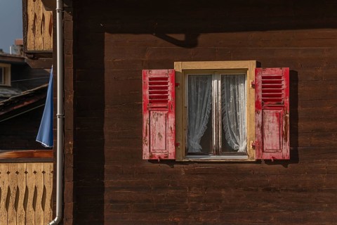 The wooden house stands in a mountain landscape, the windows are decorated with red shutters. Lace