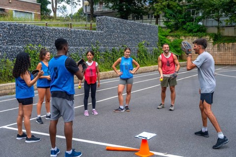 Baseball coach explaining game strategy to team players during training on an outdoor court,