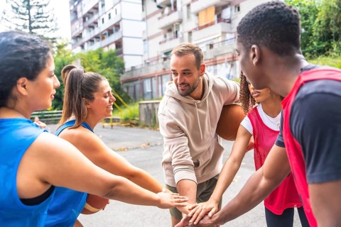 Smiling basketball players joining hands in a huddle before a street match, showcasing teamwork and