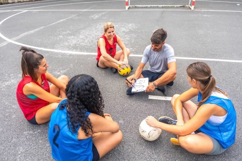 Soccer coach sitting on the field, drawing game strategy on a clipboard while female players listen