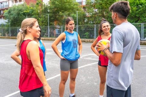 Male coach holding ball explaining game strategy to three female soccer players wearing uniforms,