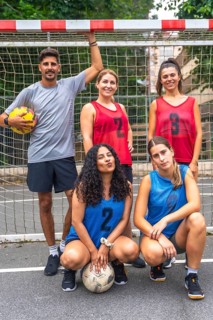 Five young soccer players, wearing numbered jerseys, are posing for a team photo on an outdoor