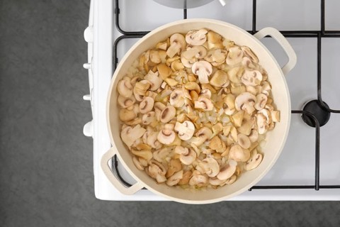 Roasting fresh mushrooms and onion in a large pan on the stove