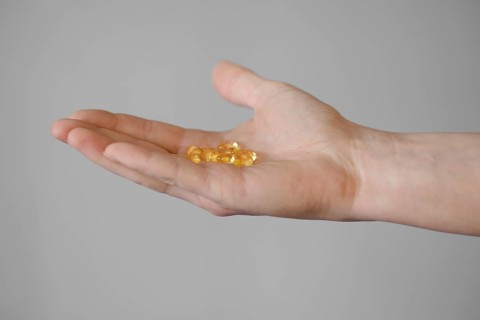 A person extends a hand, showcasing multiple yellow capsules resting on their open palm. The
