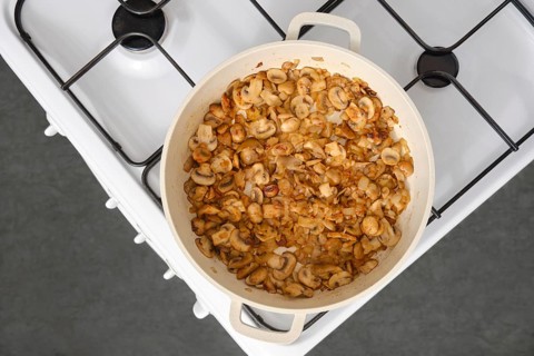 Top view of golden champignon mushrooms fried in oil in a frying pan on the stove in the kitchen