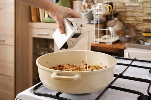 A hand pours cream over roasted mushrooms in a pot on the stove