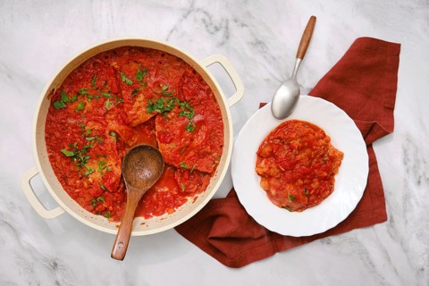 A hearty dish of pappa al pomodoro is in a pot alongside a serving on a white plate. Fresh herbs