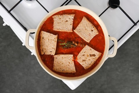 Overhead view of pot of pappa al pomodoro on a stove, filled with a vibrant red tomato broth and