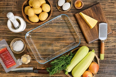 A variety of fresh ingredients are arranged on a wooden table, including potatoes, zucchini,