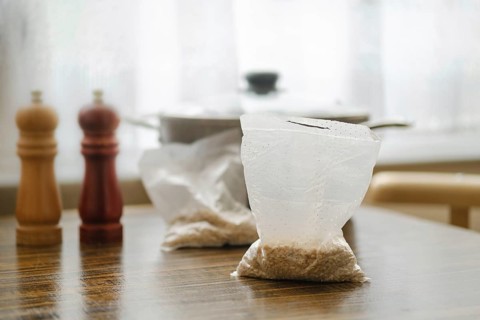 Pearl barley is prepared for cooking in convenient sachets placed on a wooden table. Nearby, salt