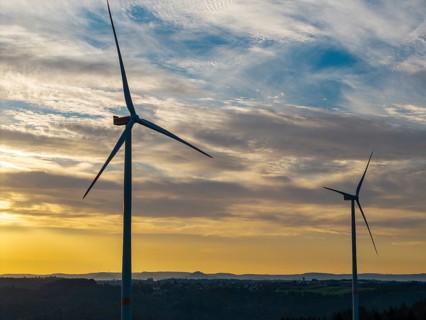 Two wind turbines turn under the early, dramatically lit clouds of a new day, near Schorndorf,