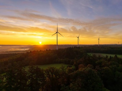 Wind turbines in a hilly and wooded landscape, illuminated by the rising sun, near Schorndorf,