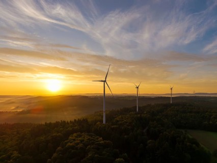 Wind turbines at dusk over wooded hills, the light gently breaking through the clouds, near