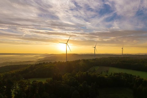 Three wind turbines above a hilly landscape, morning clouds reflecting the rising sunlight, near