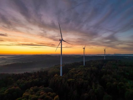 Wind turbines stand in a wooded landscape under a pastel-coloured sky at sunrise, near Schorndorf,