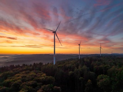 Wind turbines in the foreground of an intense pink-orange sunrise over a forest, near Schorndorf,