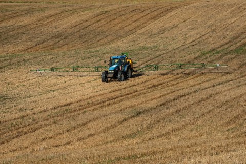Tractor spreading fertilizer on harvested stubble field in Ystad municipality, Skåne county,