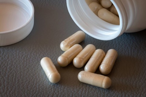 Open bottle with beige capsules and separate lid on one surface, food supplement, iron supplement,