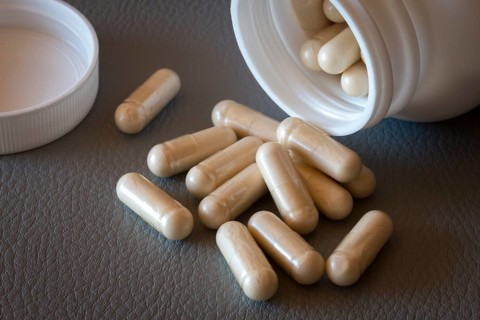 Various beige capsules taken from a half-opened bottle, food supplement, iron supplement, vitamin