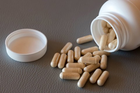 Open bottle with scattered beige capsules on a dark surface, food supplement, iron preparation,