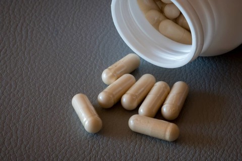 Partially emptied bottle with beige capsules on a textured surface, food supplement, iron
