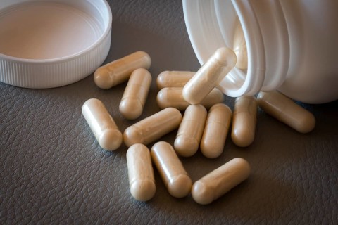 Beige capsules lying on a textured surface from an opened bottle, food supplement, iron supplement,