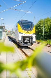 Modern white and yellow train against a green background, photographed from a distance, battery
