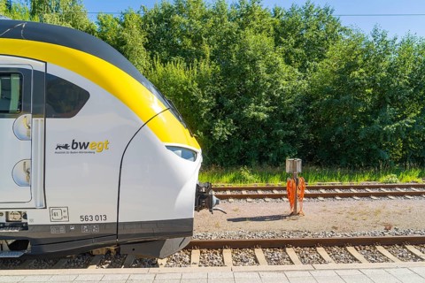 Train next to green vegetation and tracks on a sunny platform, battery Electric train with green