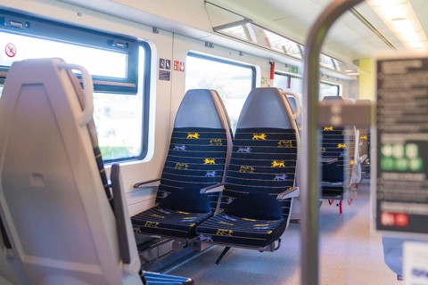 Rows of blue and yellow seats in a clean train compartment, battery Electric train with green