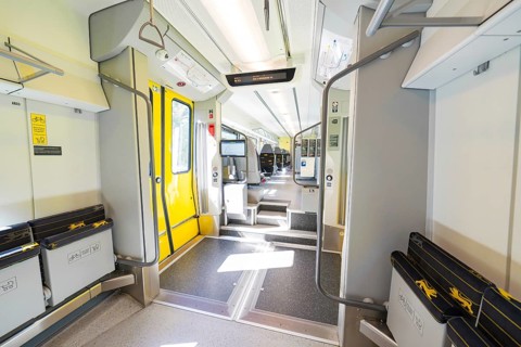 Modern and brightly lit train area with yellow doors and railings, battery Electric train with