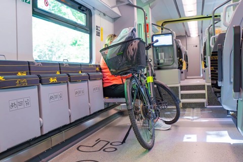 A cyclist sits in a modern, bright train compartment with his bicycle, battery Electric train with